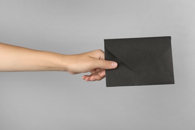 Photo of Woman holding black paper envelope on light grey background, closeup