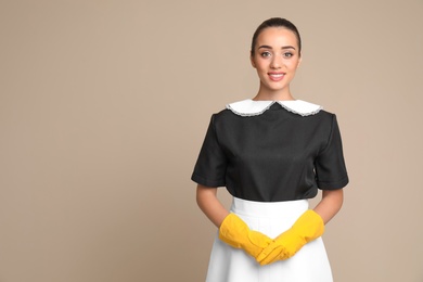 Portrait of young chambermaid in tidy uniform on color background