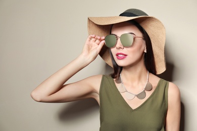 Beautiful woman in stylish sunglasses and hat on beige background