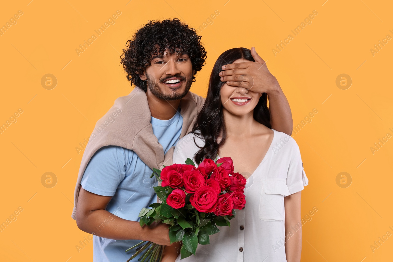 Photo of International dating. Handsome man presenting roses to his beloved woman on yellow background