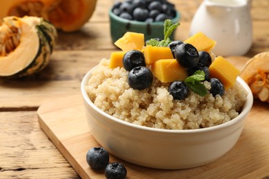 Photo of Tasty quinoa porridge with blueberries, pumpkin and mint in bowl on wooden table, closeup