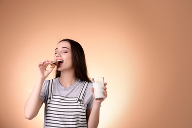 Beautiful young woman drinking milk with cookies on color background