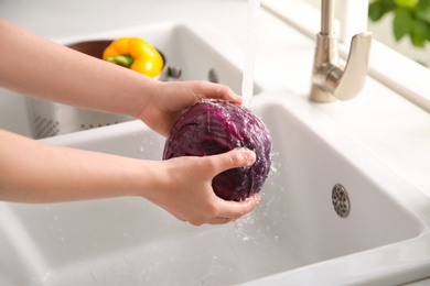 Woman washing fresh red cabbage in kitchen sink, closeup