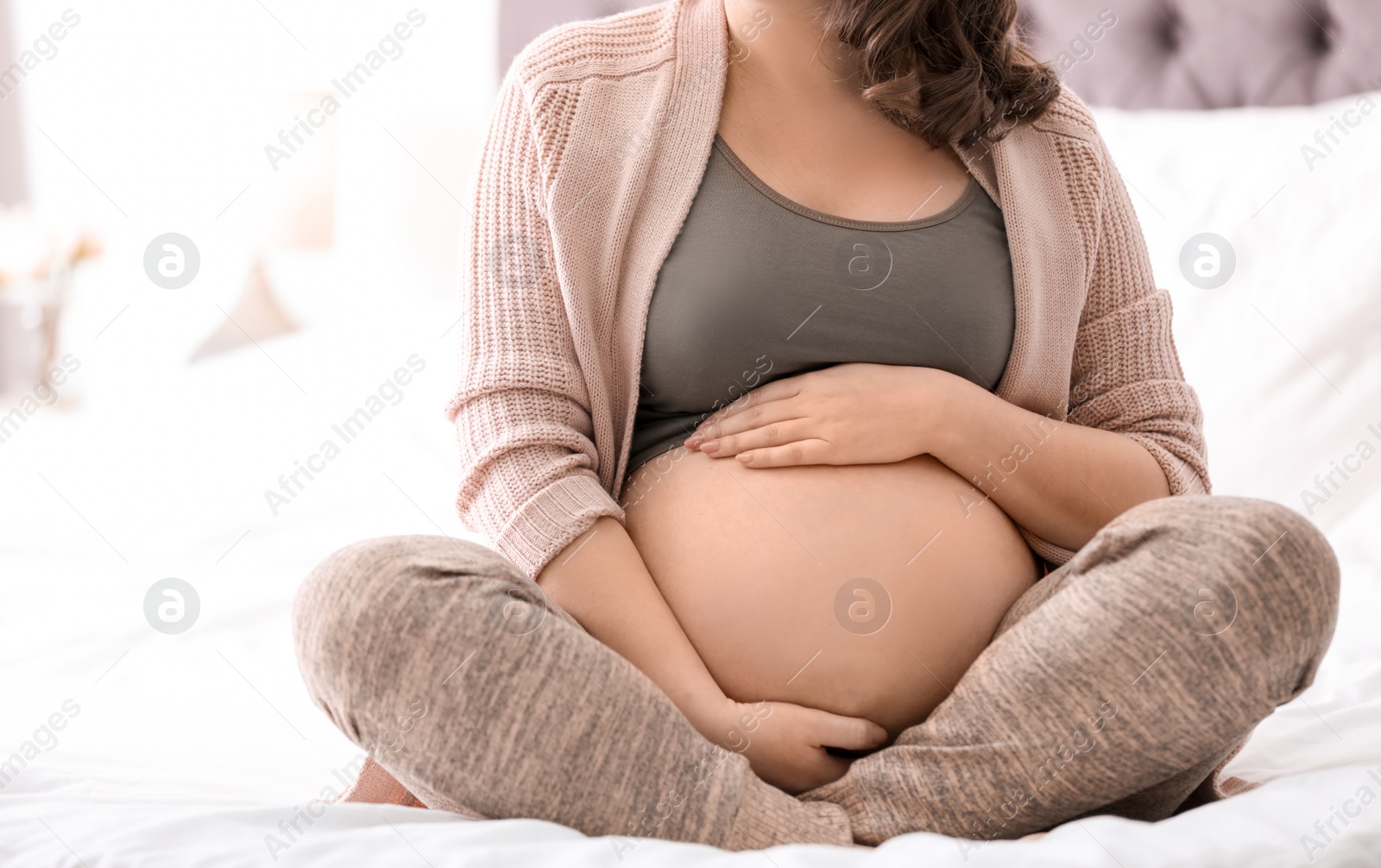 Photo of Young pregnant woman sitting on bed at home