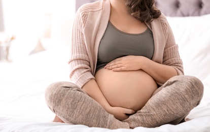 Photo of Young pregnant woman sitting on bed at home