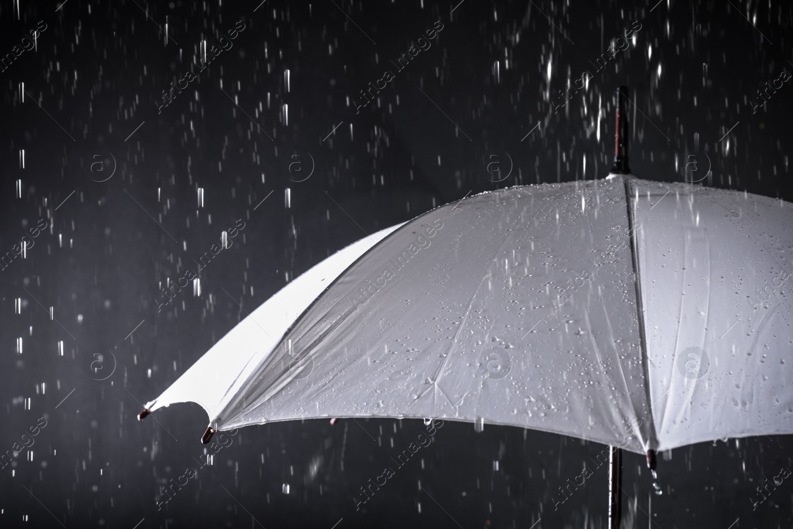 Photo of White umbrella under rain on dark background