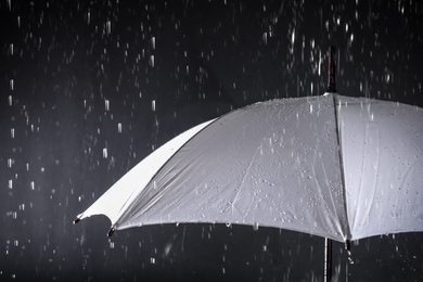 Photo of White umbrella under rain on dark background