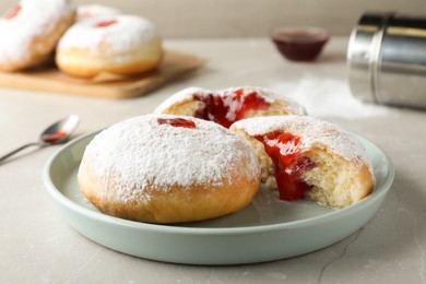 Delicious donuts with jelly and powdered sugar on light grey table, closeup