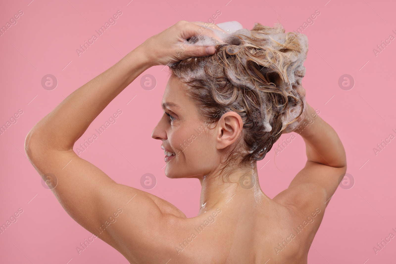 Photo of Beautiful happy woman washing hair on pink background