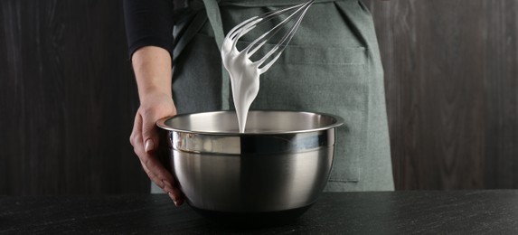 Photo of Woman making whipped cream with whisk at black table, closeup