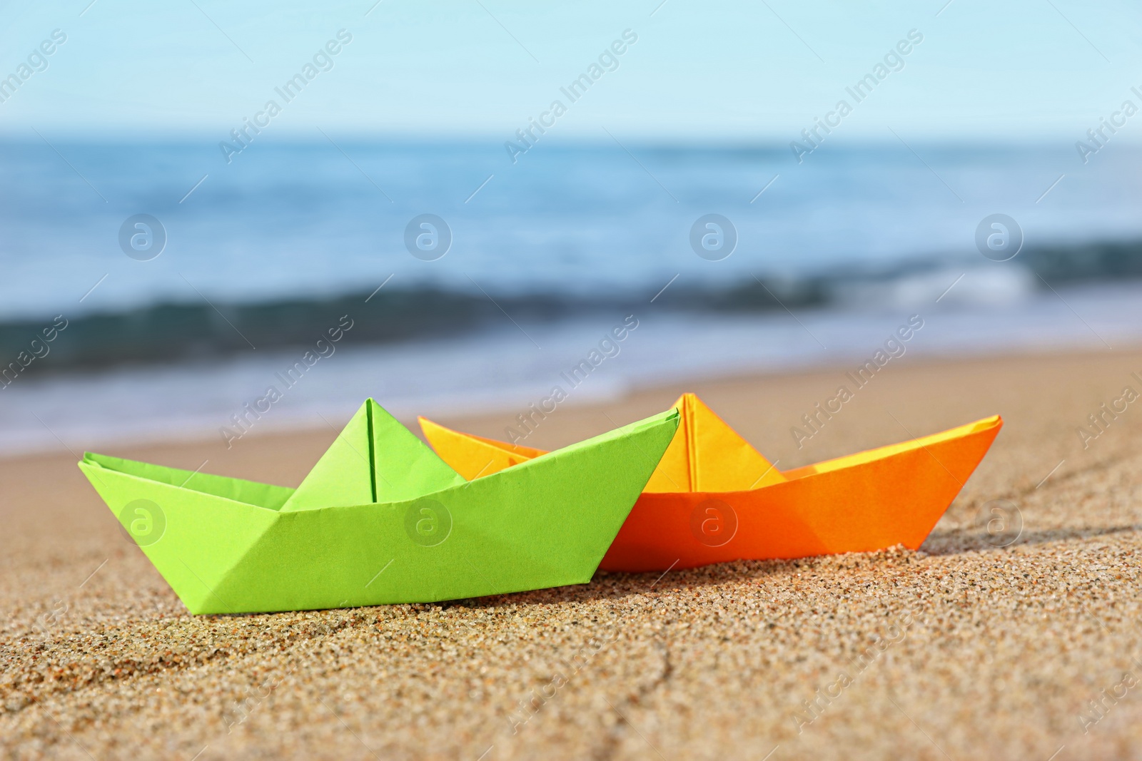 Photo of Bright color paper boats on sandy beach near sea