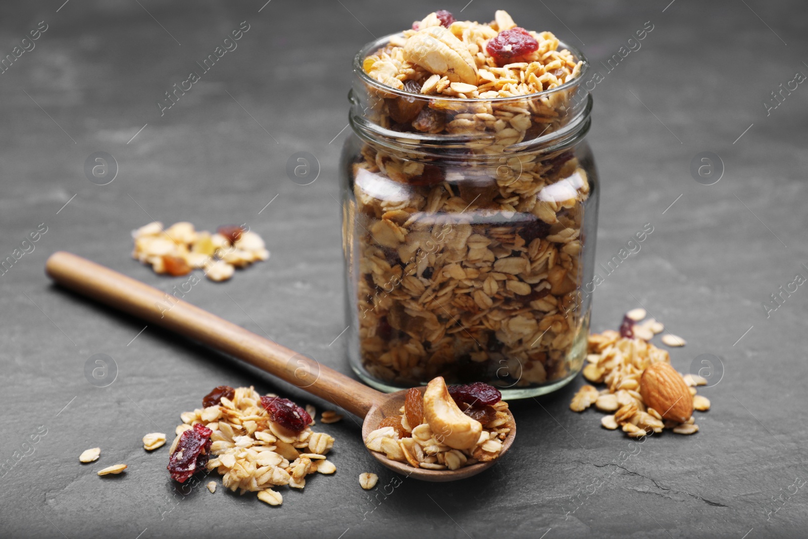 Photo of Jar of tasty granola with nuts and dry fruits on black table