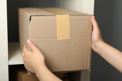 Woman putting cardboard box on shelf, closeup. Packaging goods