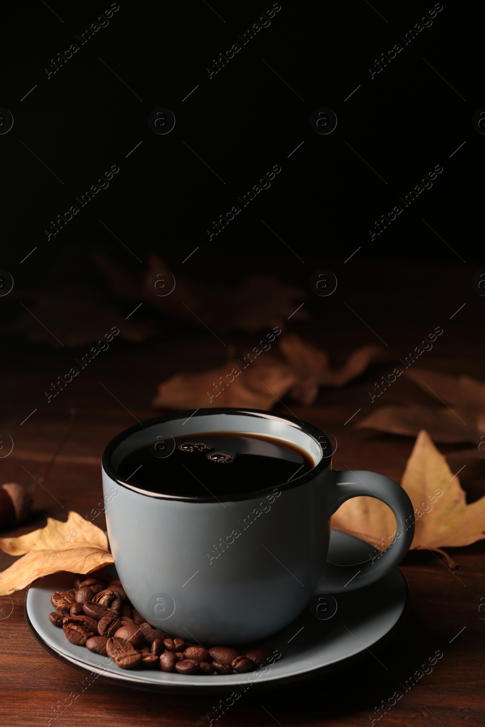 Photo of Cup of hot cozy drink with coffee beans and autumn leaves on table