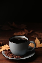 Photo of Cup of hot cozy drink with coffee beans and autumn leaves on table