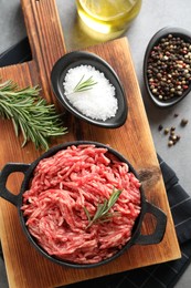 Raw ground meat in bowl, spices and rosemary on grey table, top view