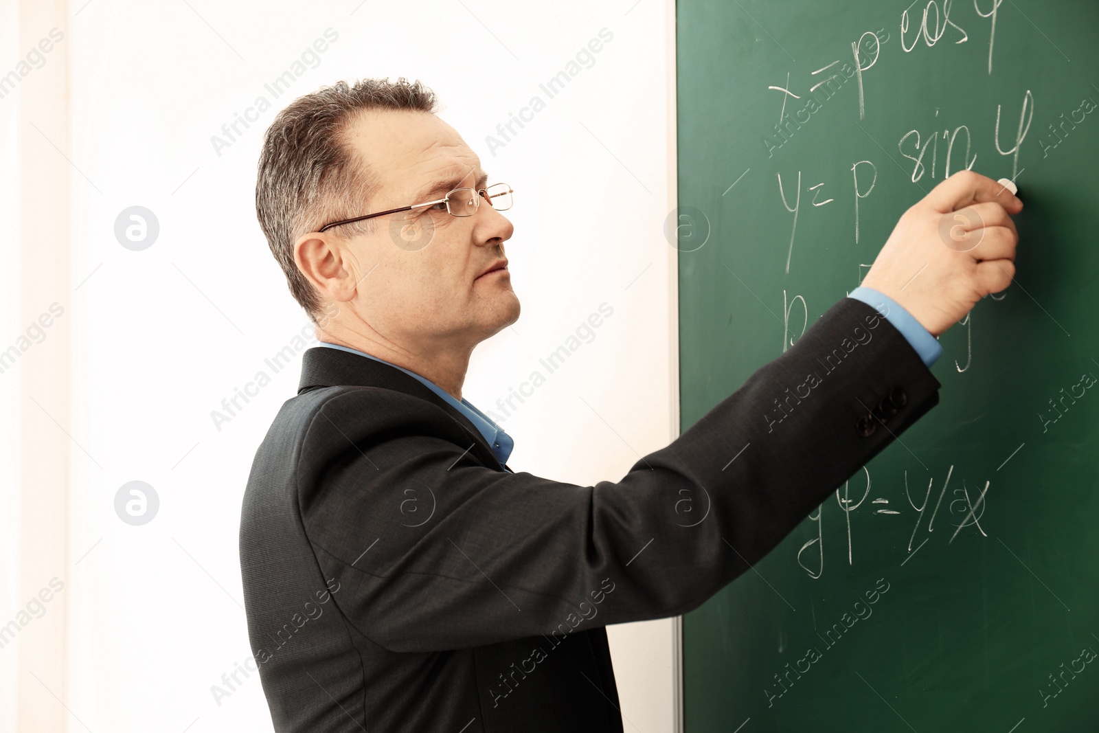 Photo of Male teacher writing on blackboard in classroom