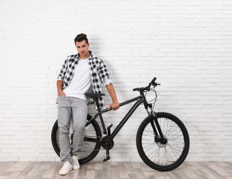 Photo of Handsome young man with modern bicycle near white brick wall indoors