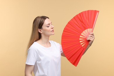 Beautiful woman waving red hand fan to cool herself on beige background