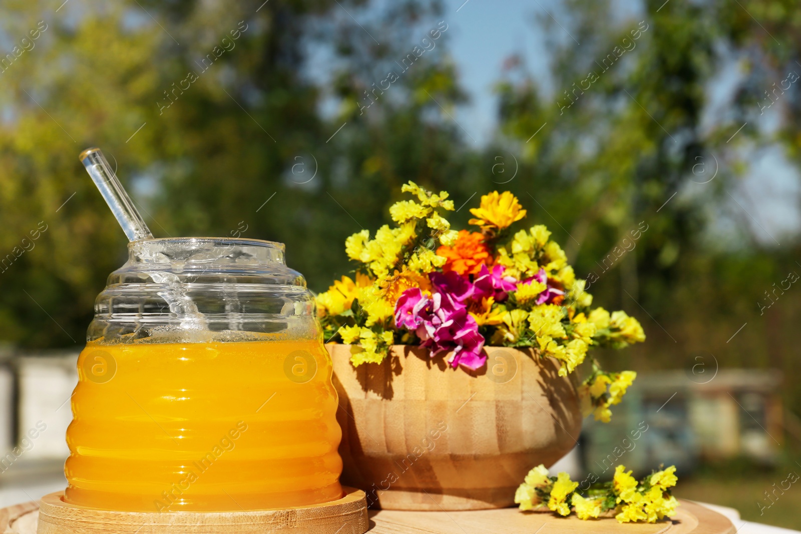 Photo of Delicious fresh honey and beautiful flowers on wooden board in apiary