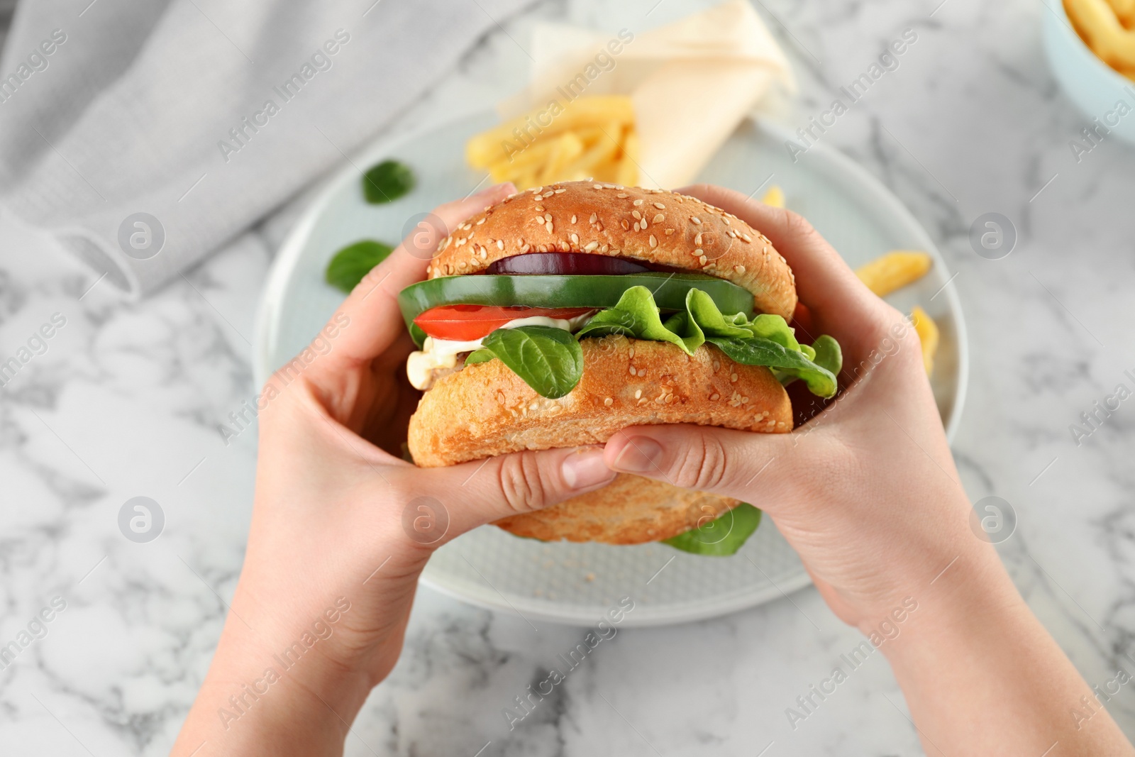 Photo of Woman holding tasty burger over plate at table, top view