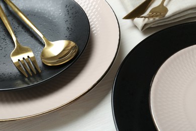 Stylish ceramic plates and cutlery on white wooden table, closeup