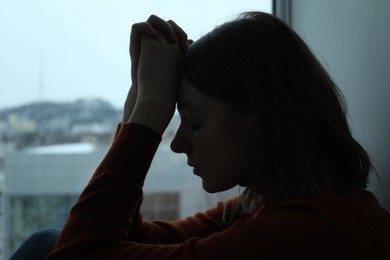Photo of Sad young woman near window at home, closeup