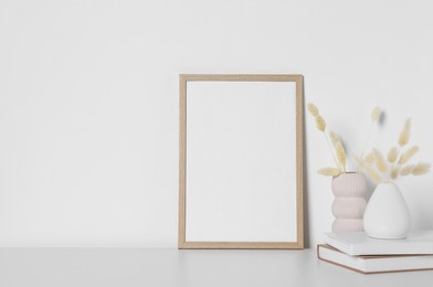 Empty photo frame and vases with dry decorative spikes on white table. Mockup for design