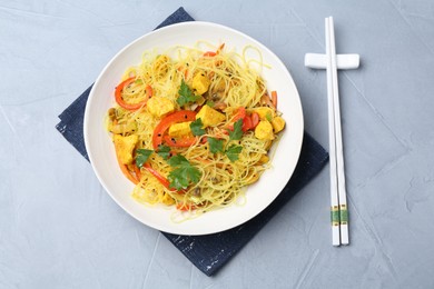 Photo of Stir-fry. Delicious cooked noodles with chicken and vegetables in bowl served on gray textured table, flat lay