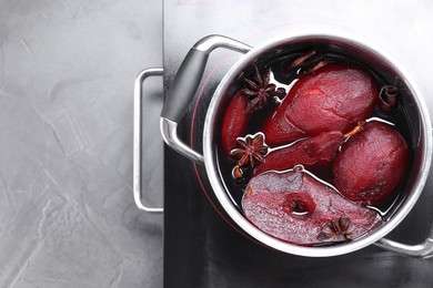 Tasty red wine poached pears and spices in pot on grey table, top view. Space for text