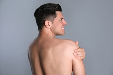 Man suffering from shoulder pain on grey background