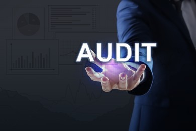 Image of Audit concept. Businessman holding digital word in hand on dark background, closeup. Graphs and charts