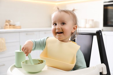 Photo of Cute little baby eating food in high chair at kitchen