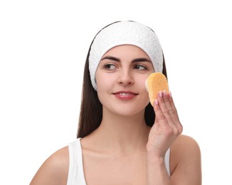 Young woman with headband washing her face using sponge on white background