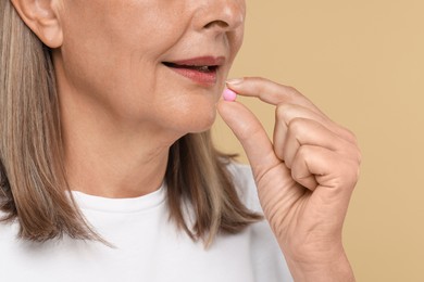 Photo of Senior woman taking pill on beige background, closeup