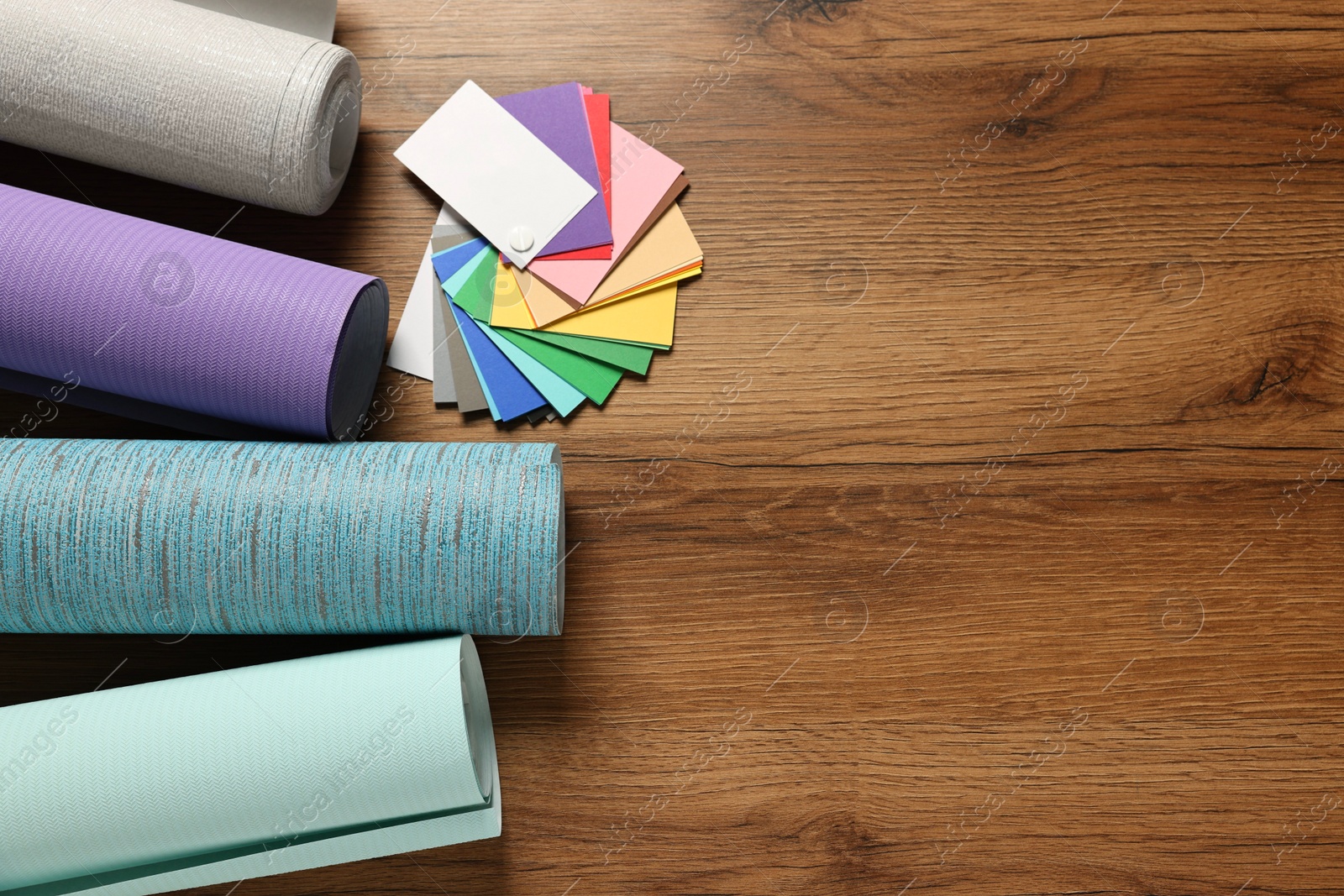 Photo of Different wallpaper rolls and color palette samples on wooden table, flat lay. Space for text