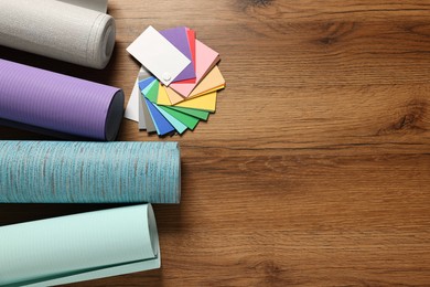 Different wallpaper rolls and color palette samples on wooden table, flat lay. Space for text