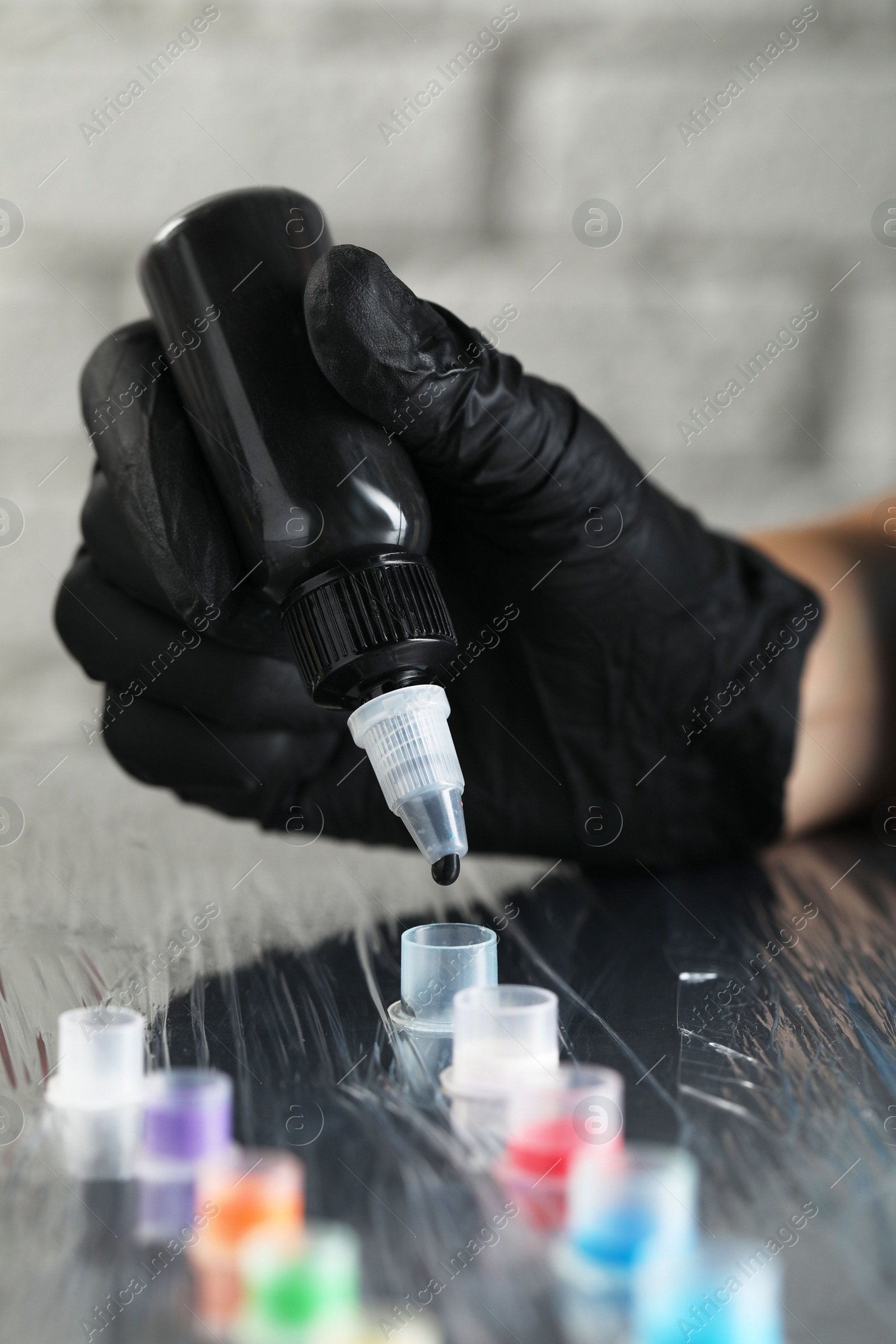 Photo of Tattoo artist dripping black tattoo ink into cap on table, closeup