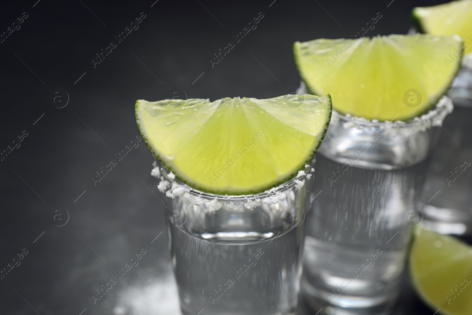 Photo of Mexican Tequila shots, lime slices and salt on table, closeup