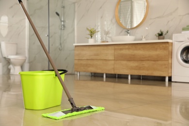 Photo of Bucket and mop on floor at home, space for text. Cleaning equipment