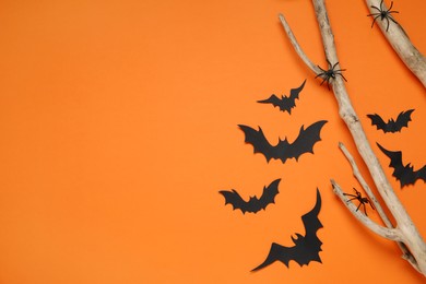 Flat lay composition with paper bats, spiders and wooden branches on orange background, space for text. Halloween decor