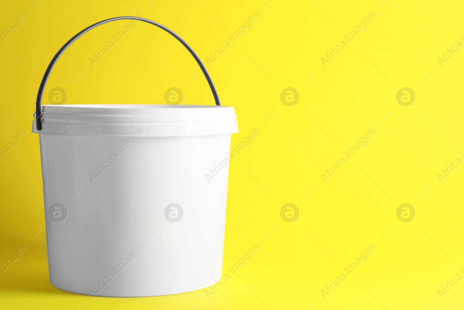 Photo of One plastic bucket with lid on yellow background. Space for text