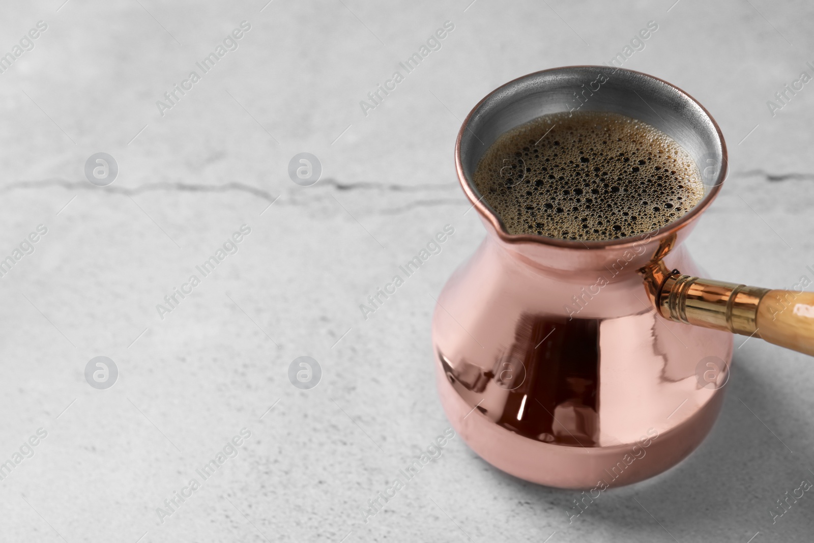 Photo of Turkish coffee in cezve on light grey table. Space for text