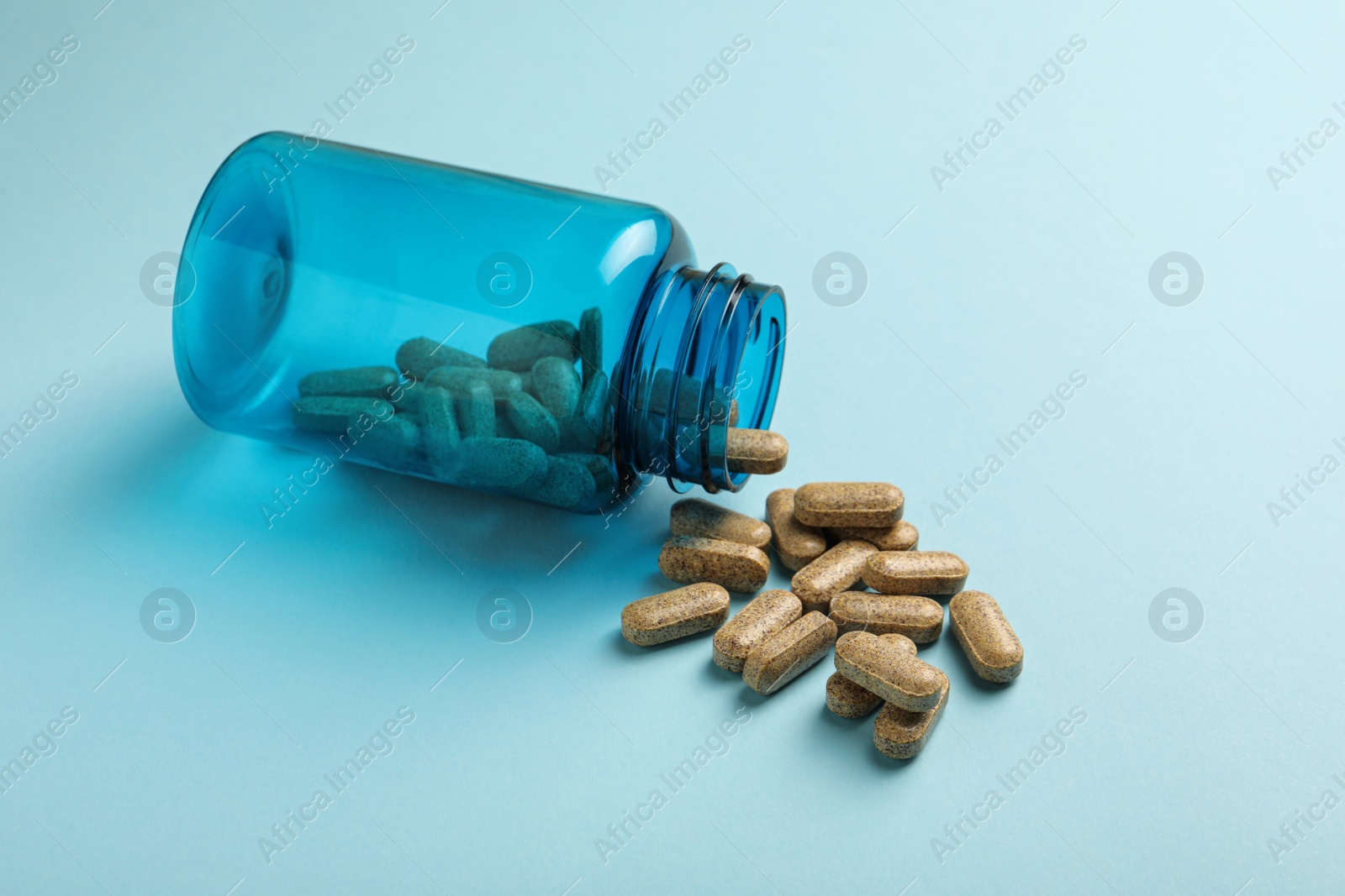 Photo of Overturned bottle with dietary supplement pills on light blue background