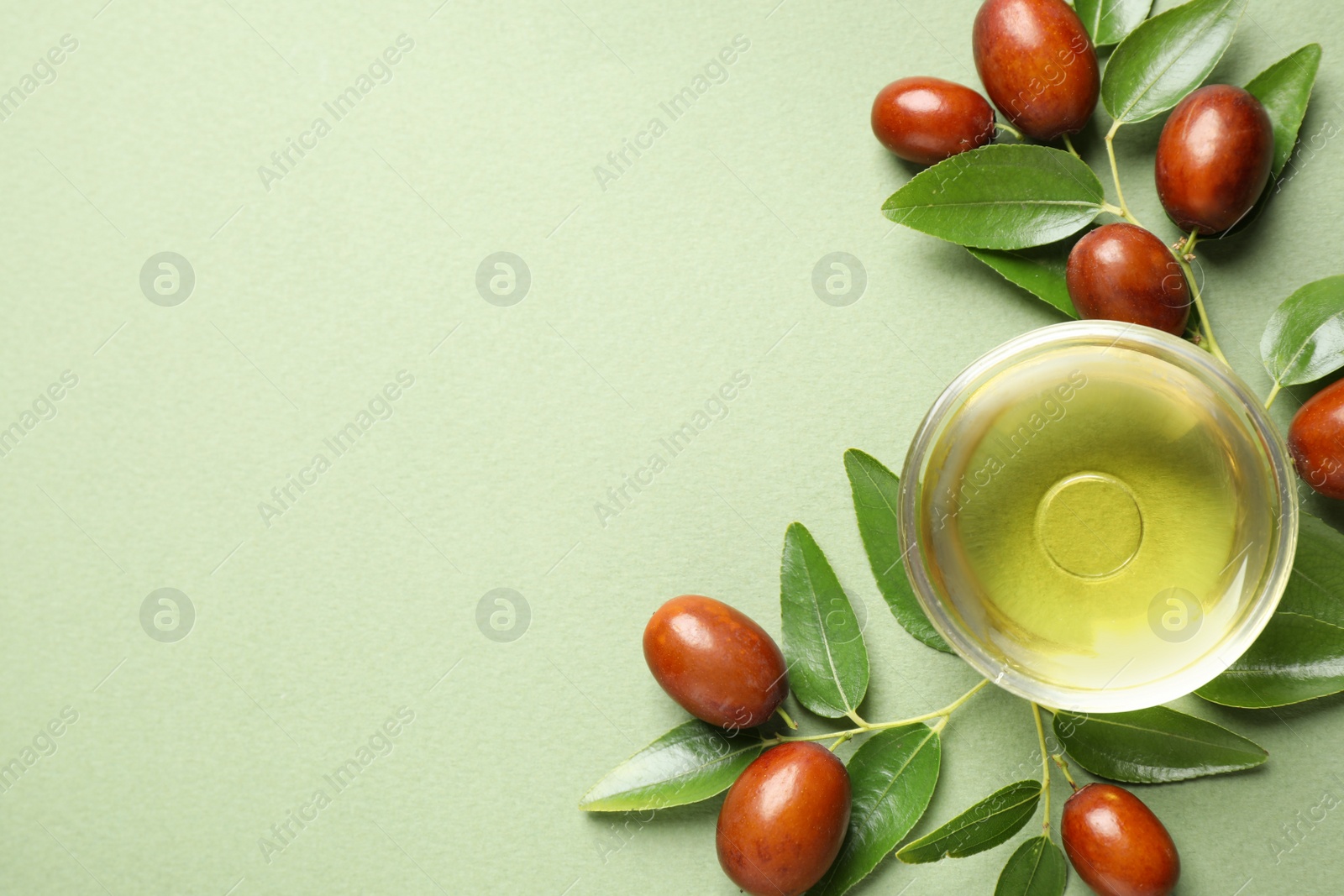 Photo of Glass bowl with jojoba oil and seeds on green background, flat lay. Space for text