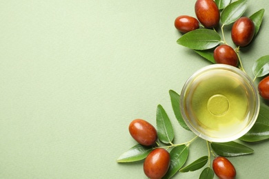 Glass bowl with jojoba oil and seeds on green background, flat lay. Space for text