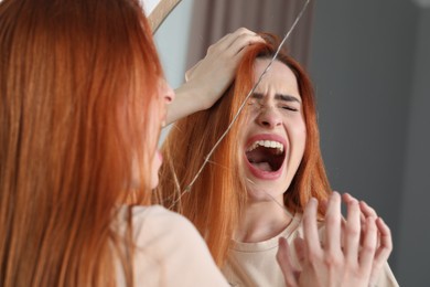 Mental problems. Young woman screaming near broken mirror indoors