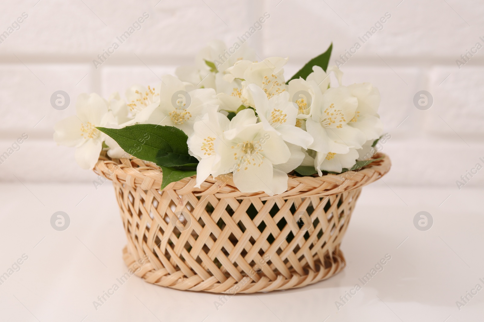 Photo of Beautiful jasmine flowers in wicker basket on white table