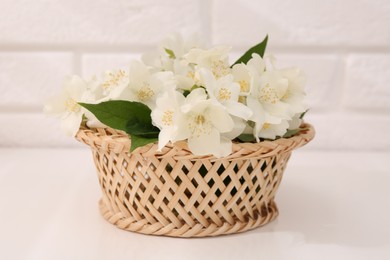 Beautiful jasmine flowers in wicker basket on white table