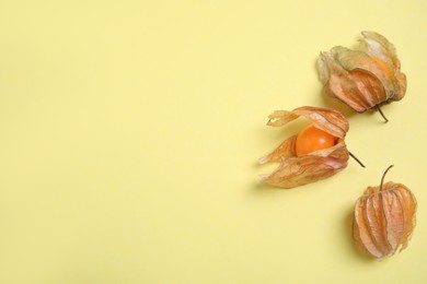 Photo of Ripe physalis fruits with dry husk on yellow background, flat lay. Space for text